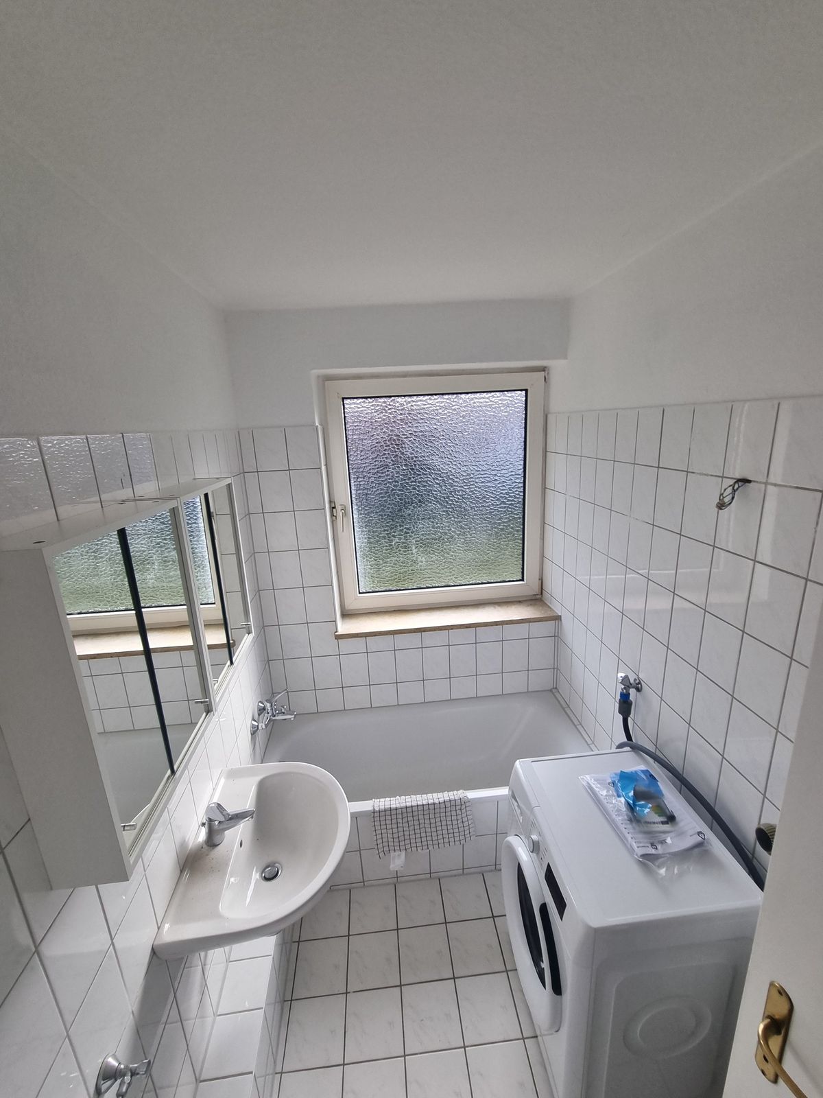 Helles Bad mit Badewanne, Waschbecken, Spiegelschrank und Waschmaschine